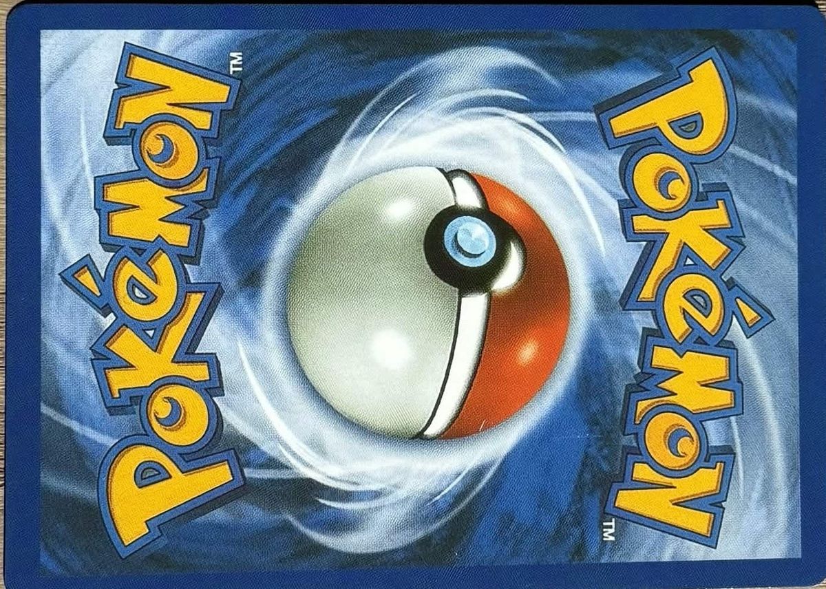 Back of a counterfeit Pokémon card on the same table: lighter, grayer border, softer swirl.
