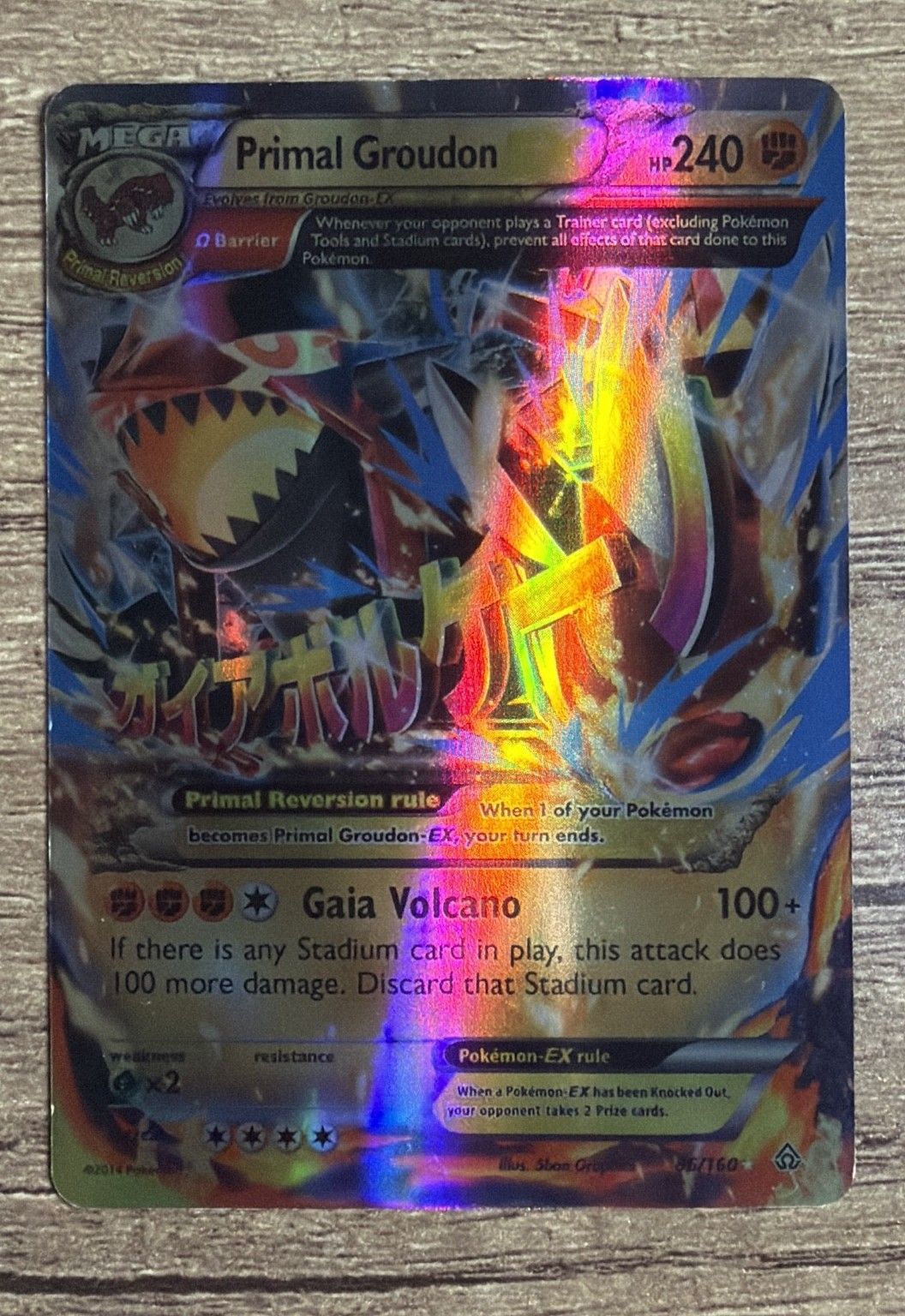 A genuine Primal Groudon EX under a lamp: a broad, soft rainbow sweep across the whole face.