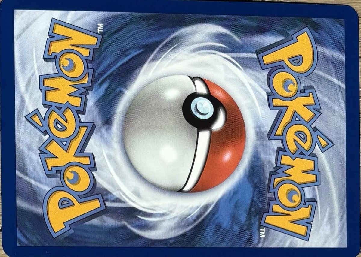 Back of a genuine Pokémon card on a wooden table: navy border, crisp swirl around the Poké Ball.