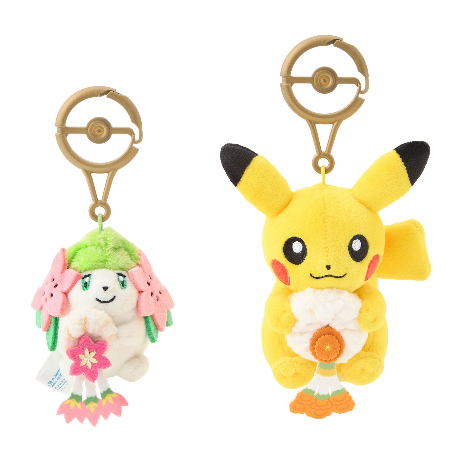 Two small plush keychains on gold Poké Ball clips: Shaymin holding a white garland with a pink flower, and Pikachu holding a white garland with an orange flower.