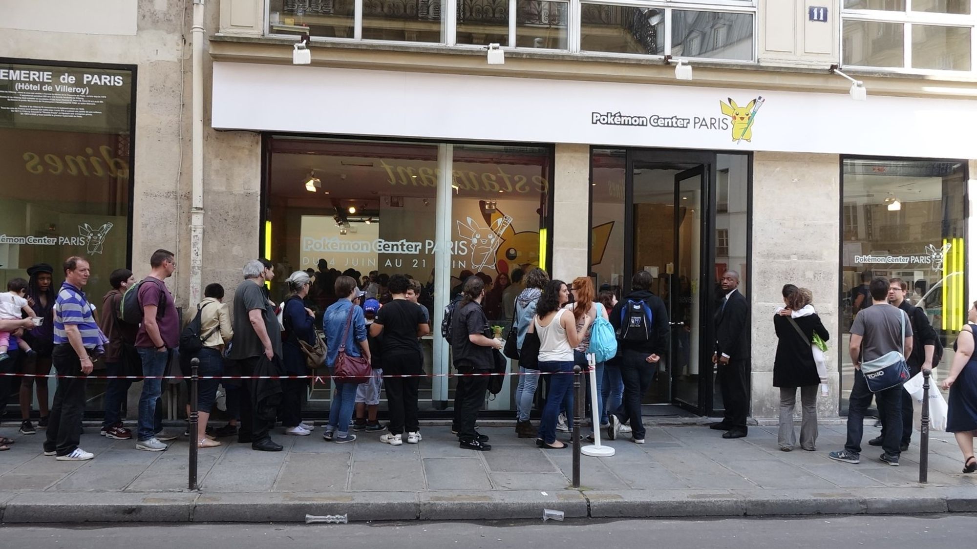 A queue on the sidewalk outside Pokémon Center Paris in 2014, under an awning reading Pokémon Center PARIS with a Pikachu.