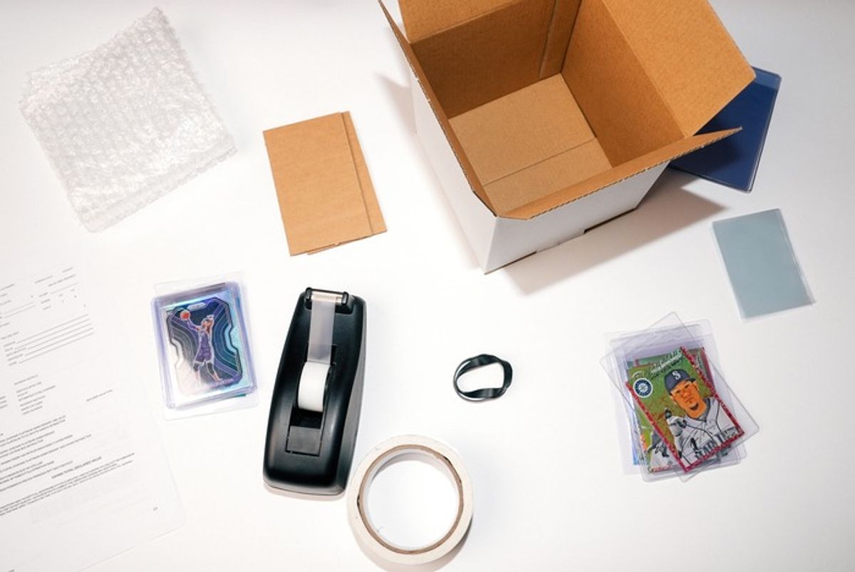 Flat lay of the shipping materials PSA requires: box, bubble wrap, tape, rubber band, submission form and cards already in semi-rigid holders.